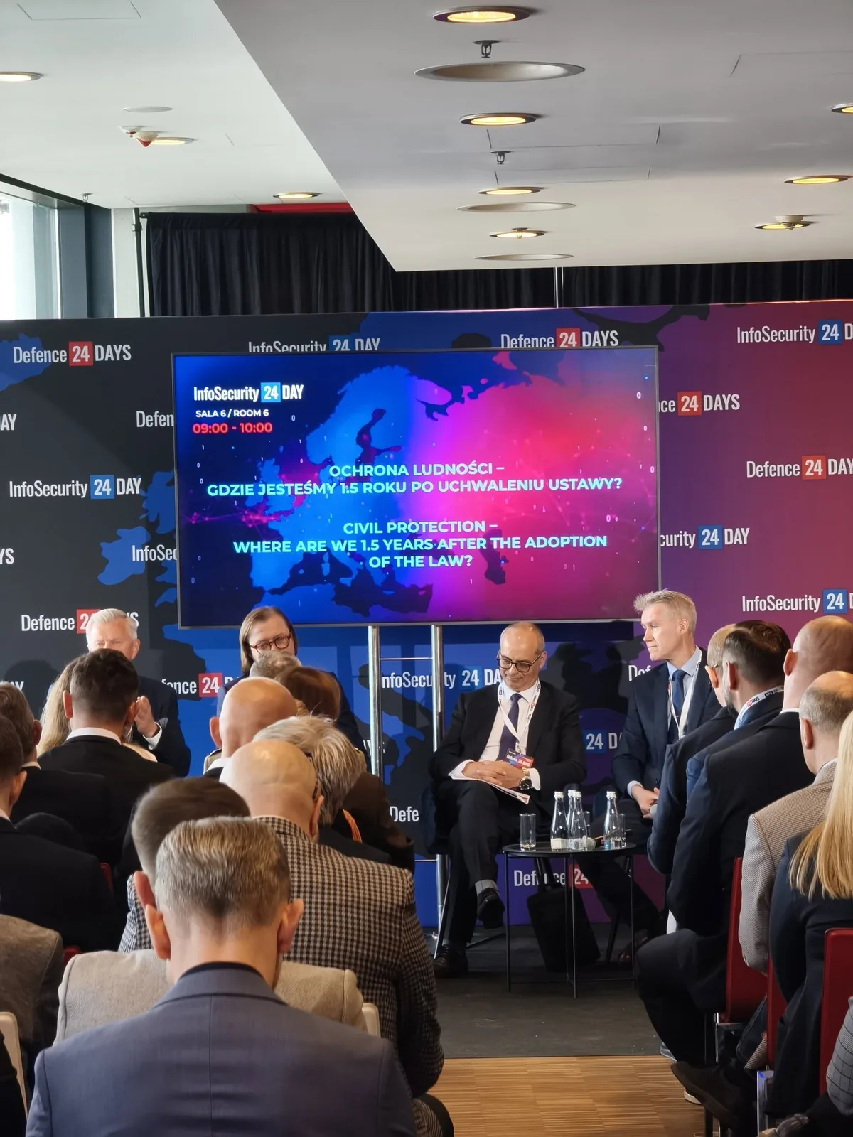 Paneliści i publiczność przed ekranem z tytułem dyskusji o ochronie ludności.