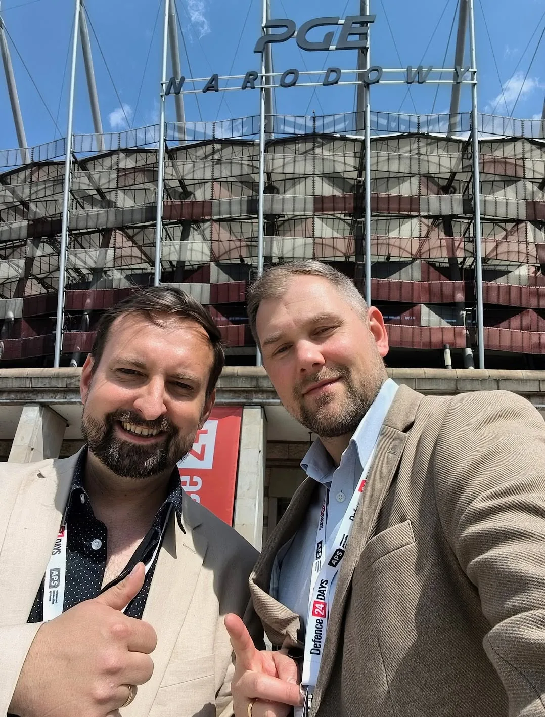 Dwóch uczestników z identyfikatorami Defence24 Days przed stadionem PGE Narodowy.